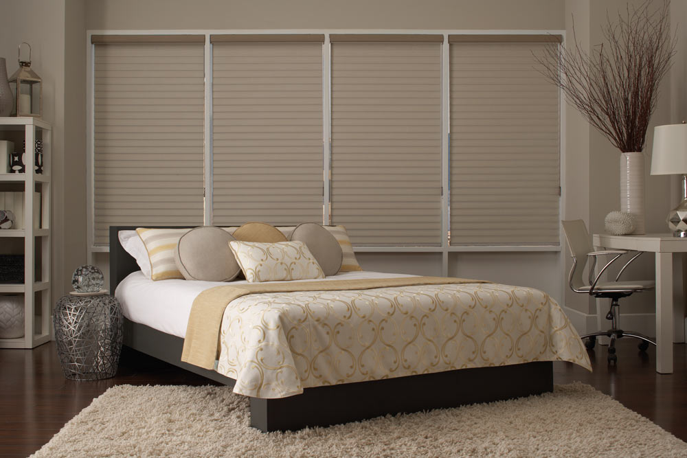 several tan Tenera® Sheer Shades behind a large bed with tan and yellow Interior Masterpieces® Custom Bedding and Pillows