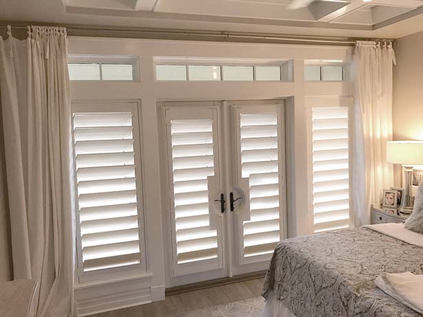 White Parke Shutters® with French Door Cutouts in a bedroom with a bed and draperies