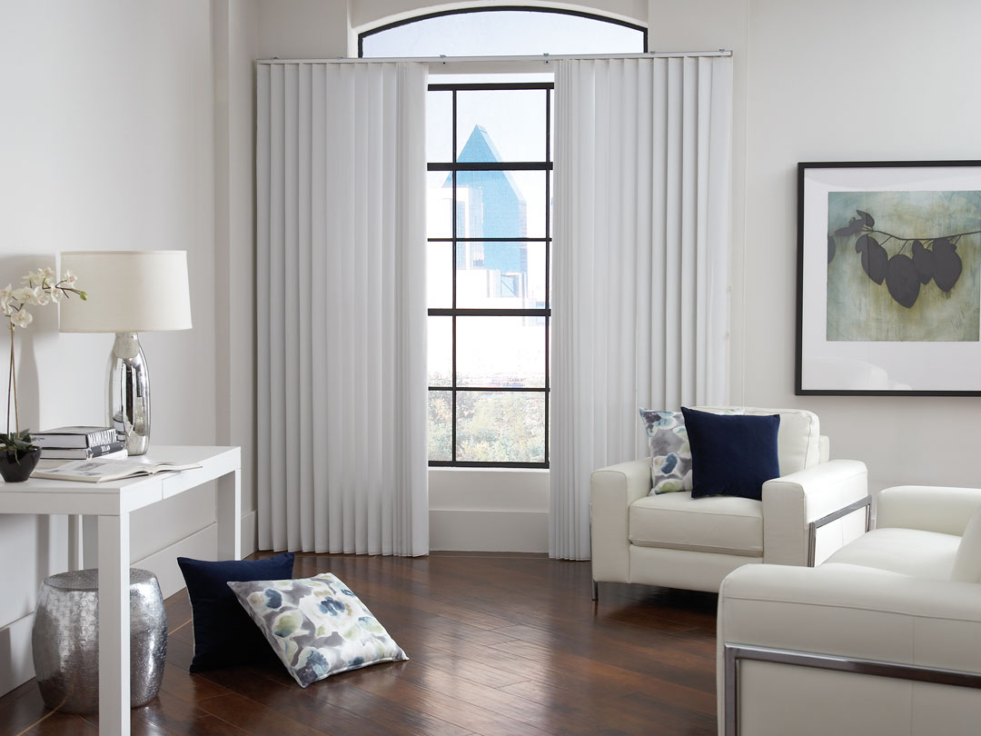White Sheer Visions® Vertical Blinds hanging in a window in a room with wood floors and white furniture around and custom Interior Masterpieces® pillows