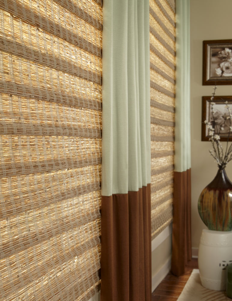 close up of light brown and dark brown Manh Truc® Woven Wood Shades and light green and dark brown Interior Masterpieces® Draperies