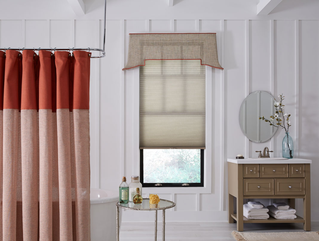 tan Parasol® Cellular Shades & Interior Masterpieces® Fabric Cornice with red trim in a bathroom with a red shower curtain and brown vanity