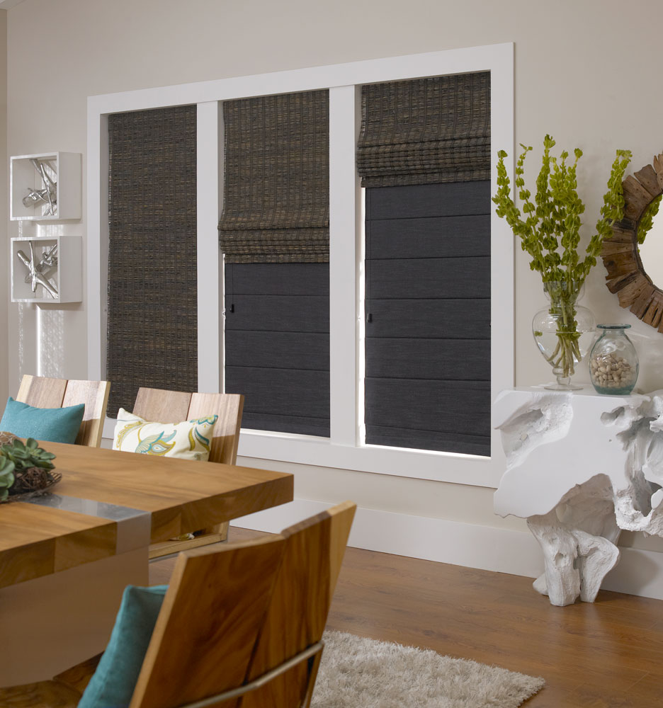 Three dark Manh Truc® Duo-Fold Woven Wood Shades in different raised positions showing the room darkening liner behind the Woven Wood Shade
