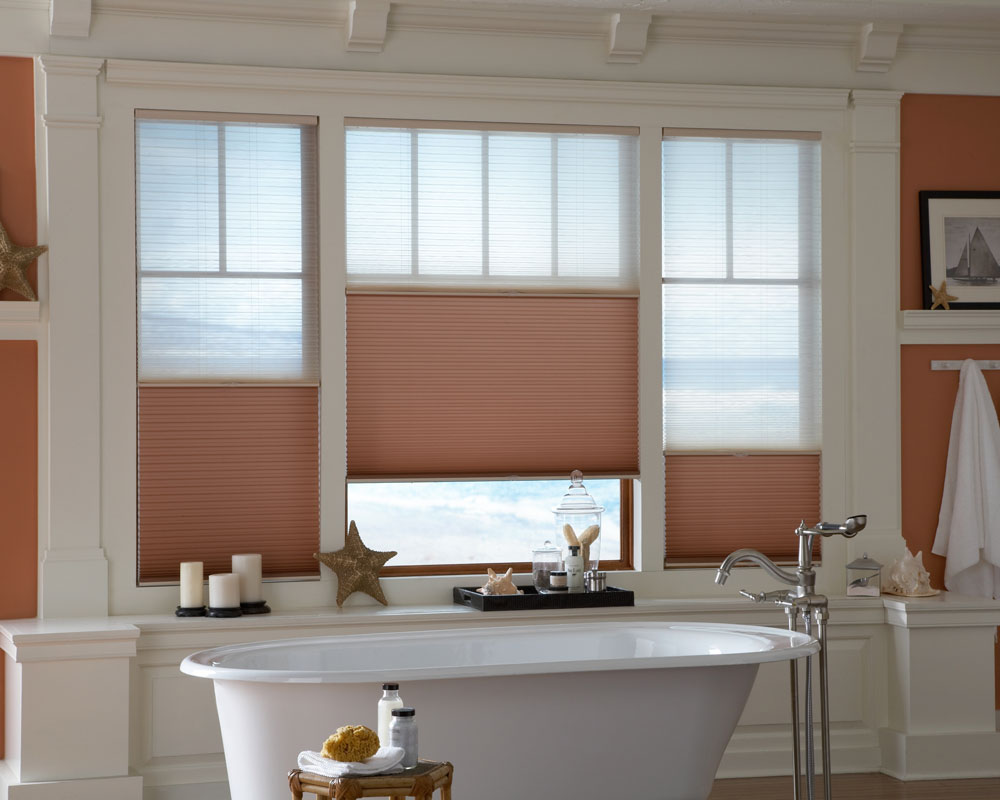 3 red and tan Parasol® Duo-Lucent Cellular Shades in a large bathroom picture window behind a large white stand alone bath tub
