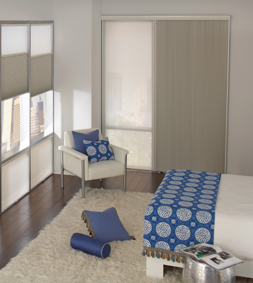 Two toned cellular shades hang horizontally in two windows and vertically on a large window for easy sliding in a high-rise bedroom featuring custom blue medallion patterned bedding.