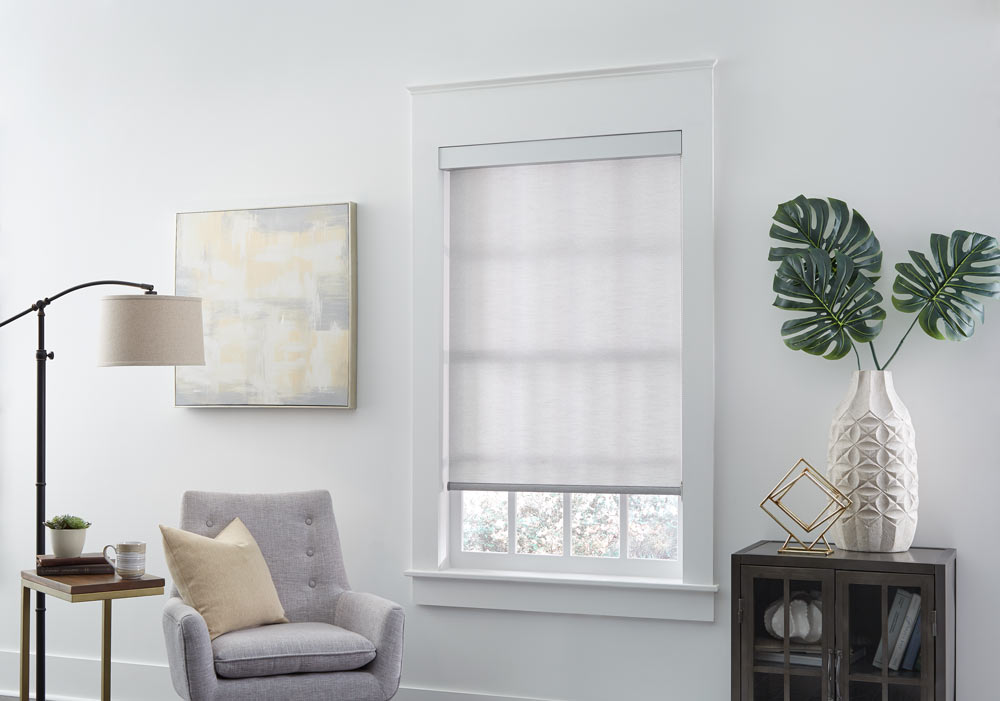 gray Genesis® Roller Shade next to a light gray chair with a tan pillow on it
