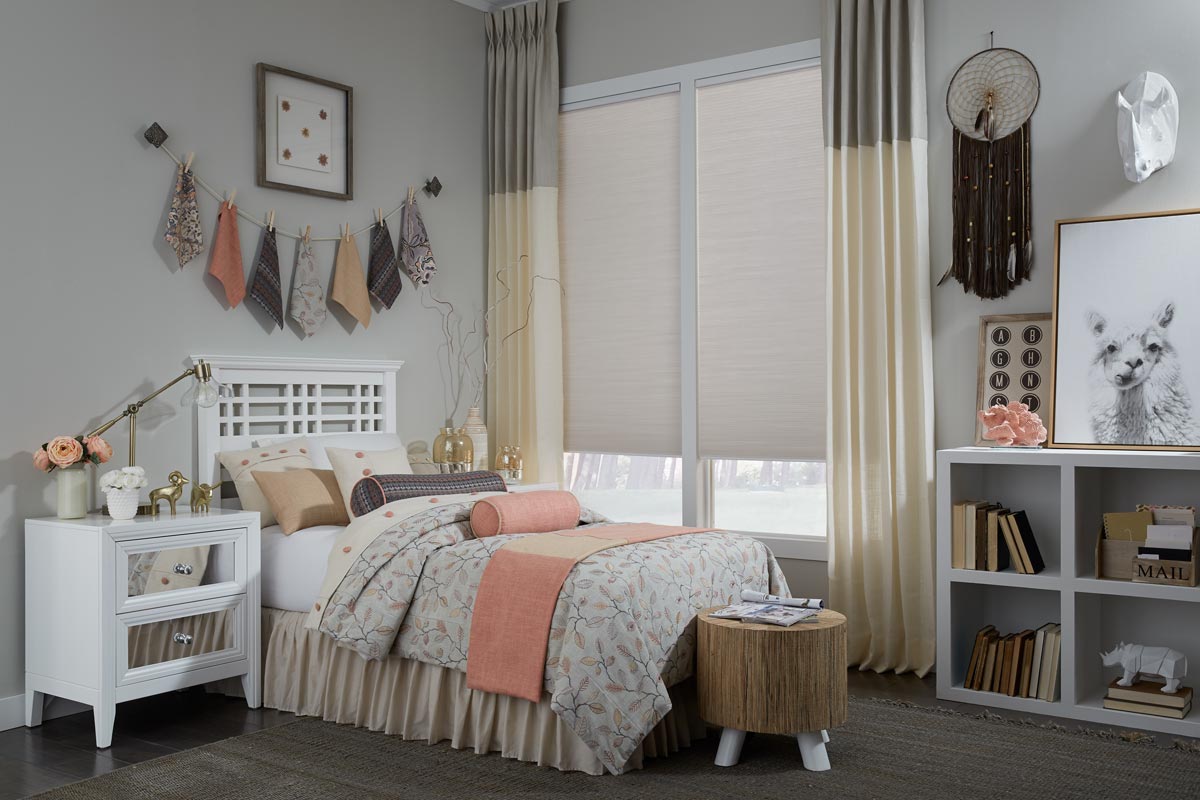 Custom Interior Masterpieces® Stationary Draperies hung in a window with a fabric shade in front of a bed that has custom bedding and accessories