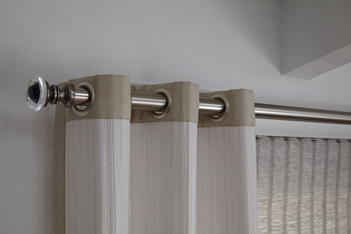 A white Manh Truc® Woven Wood Grommet Panel with silver Custom Hardware and tan Banding with a tan colored grass Genesis® Roman Shade