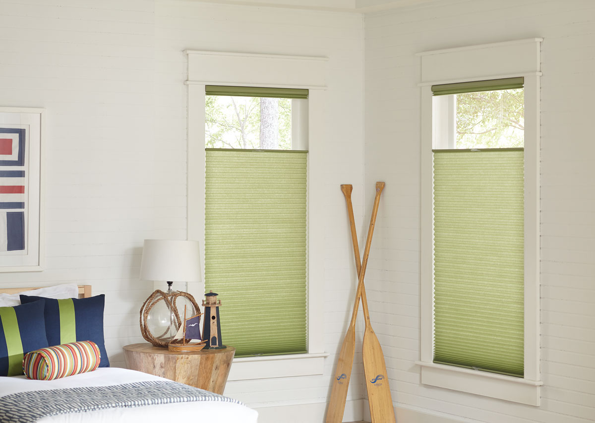 Two green Parasol® Cellular Top Down/Bottom Up lifting systems in a bedroom with accenting blue and green pillows on a gray bed and nautical decorations in the room