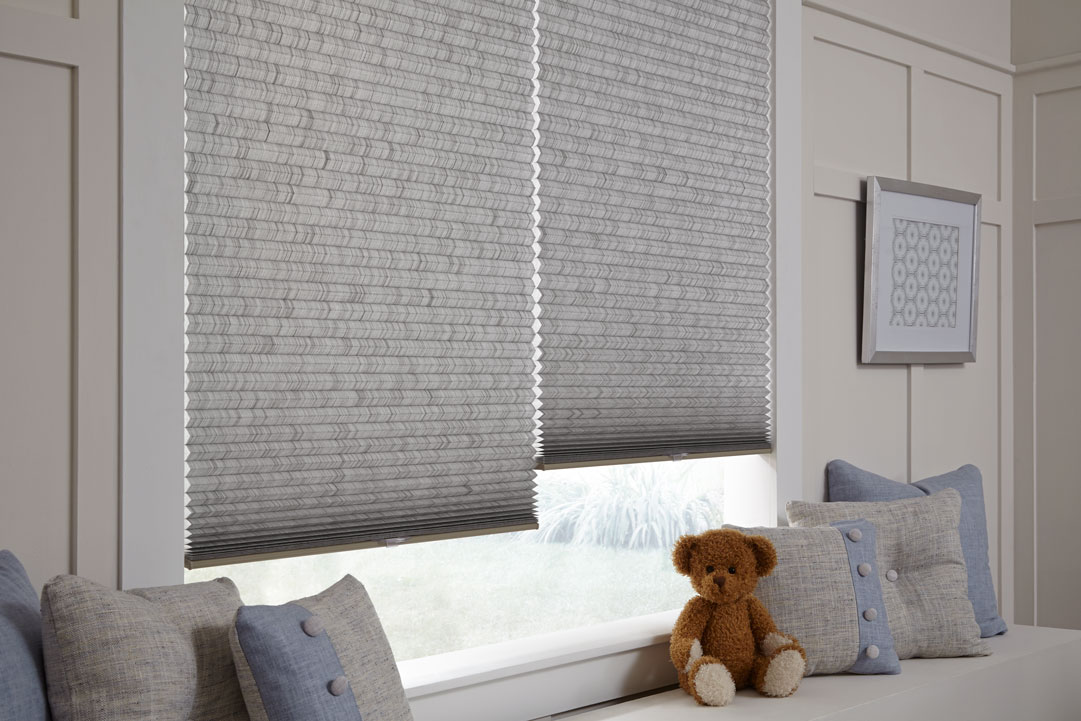 close up view of some gray Parasol® Cellular Shades with matching Interior Masterpieces® Custom Pillows on a bench and a brown teddy bear in between them