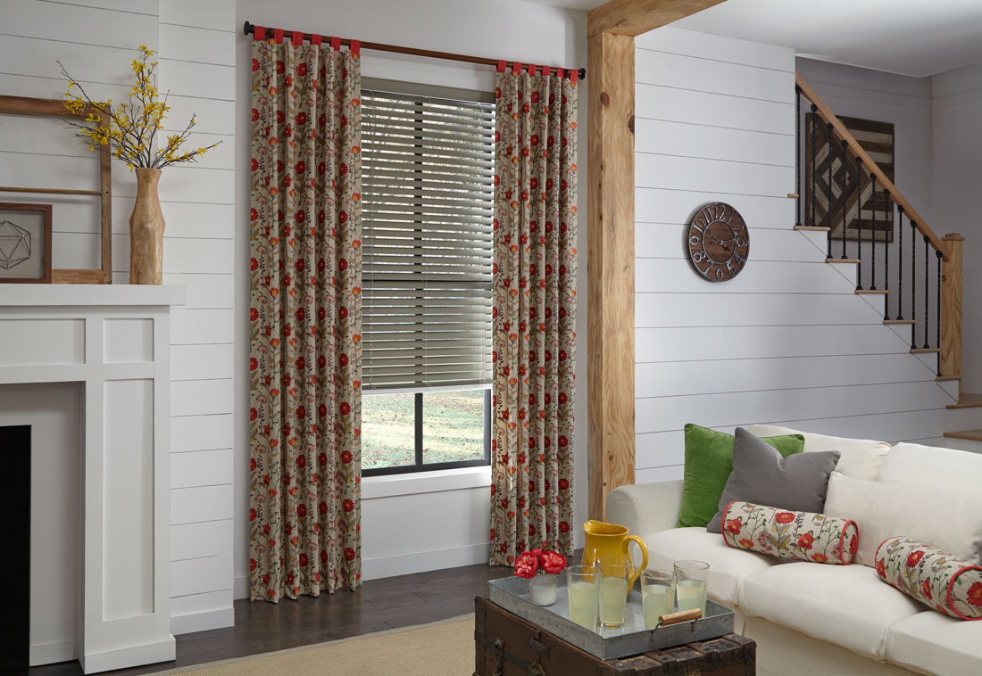 Gray Wonderwood® Wood Blinds with Interior Masterpieces® Draperies in a red floral pattern with Custom Hardware behind a white couch with Custom Pillows