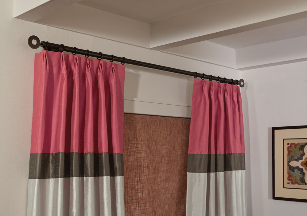 color block Interior Masterpieces® draperies in pink, dark brown and light gray hanging on a black custom rod with rings and finials in front of a red fabric shade