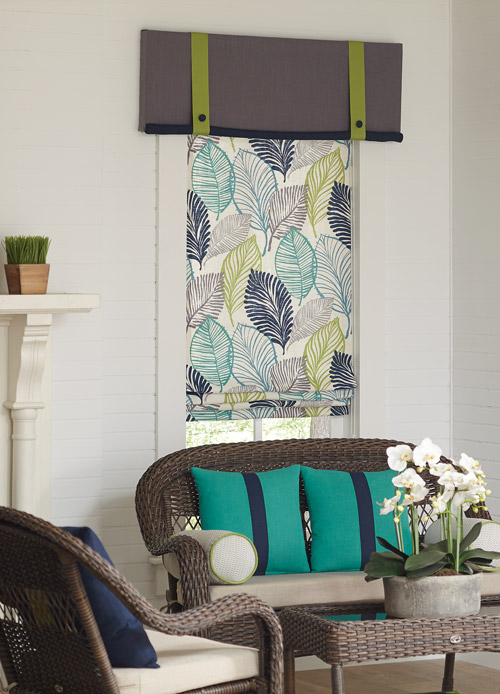 Floral teal, blue, and yellow Interior Masterpieces® fabric shade with gray and green custom cornice behind a chair with teal and blue accenting pillows