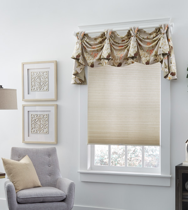 Custom Rod Mounted Interior Masterpieces® valance above a tan cellular shade in a room with white walls and a chair with a custom accent pillow