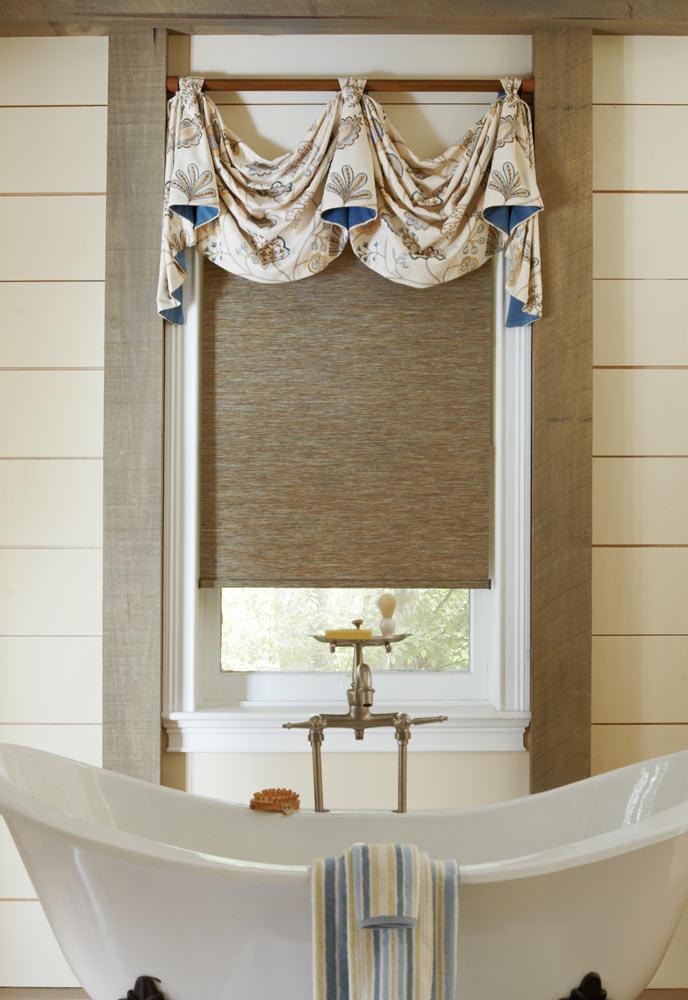 brown Genesis® Custom Roller Shade with a white and blue floral patterned Interior Masterpieces® Fabric Valance behind a white stand alone tub