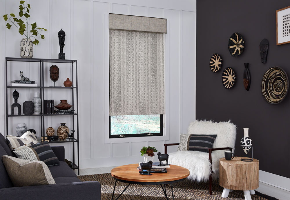 Tan and black patterened Interior Masterpieces® fabric shade with matching fabric cornice in a room with a fluffy chair and couch with accenting custom pillows