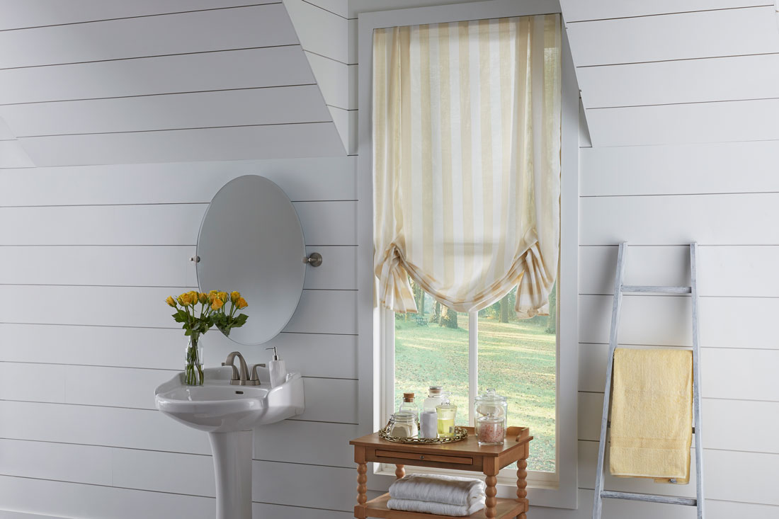 Yellow and white Interior Masterpieces® fabric shade in a bathroom with yellow flowers on a sink and a brown table in front