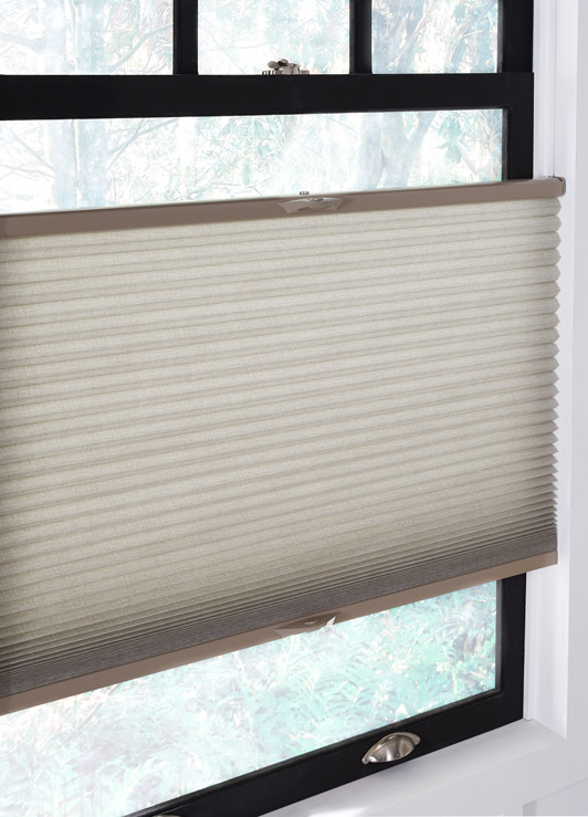 A top down bottom up cellular shades hangs in a window, slightly ajar from both the top and bottom.