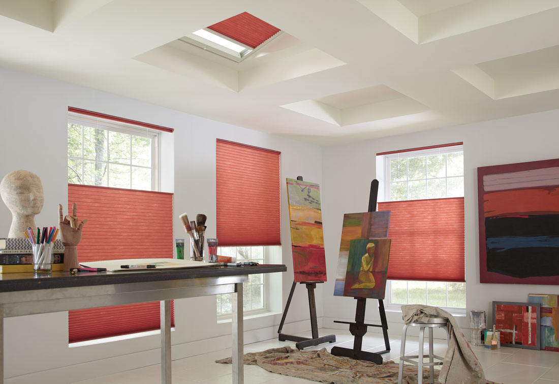 Three red Parasol® Top Down-Bottom Up shades in windows with a Parasol SkyLight shade in the ceiling in a studio room with painting supplies and paintings nearby
