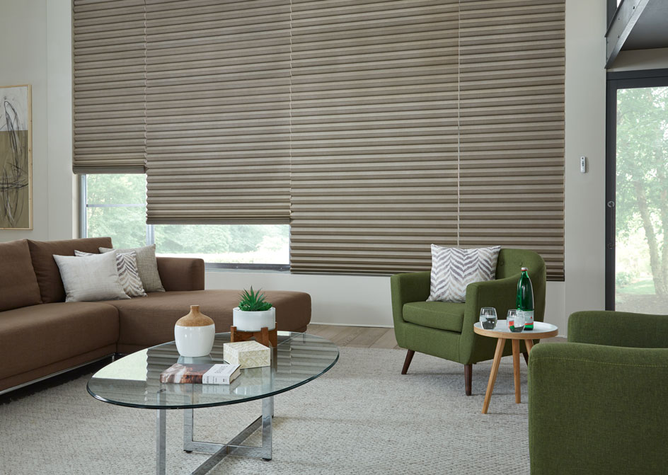 4 large Motorized Parasol® Cellular Shades in a large picture window in a living room with a brown couch and a green chair in front