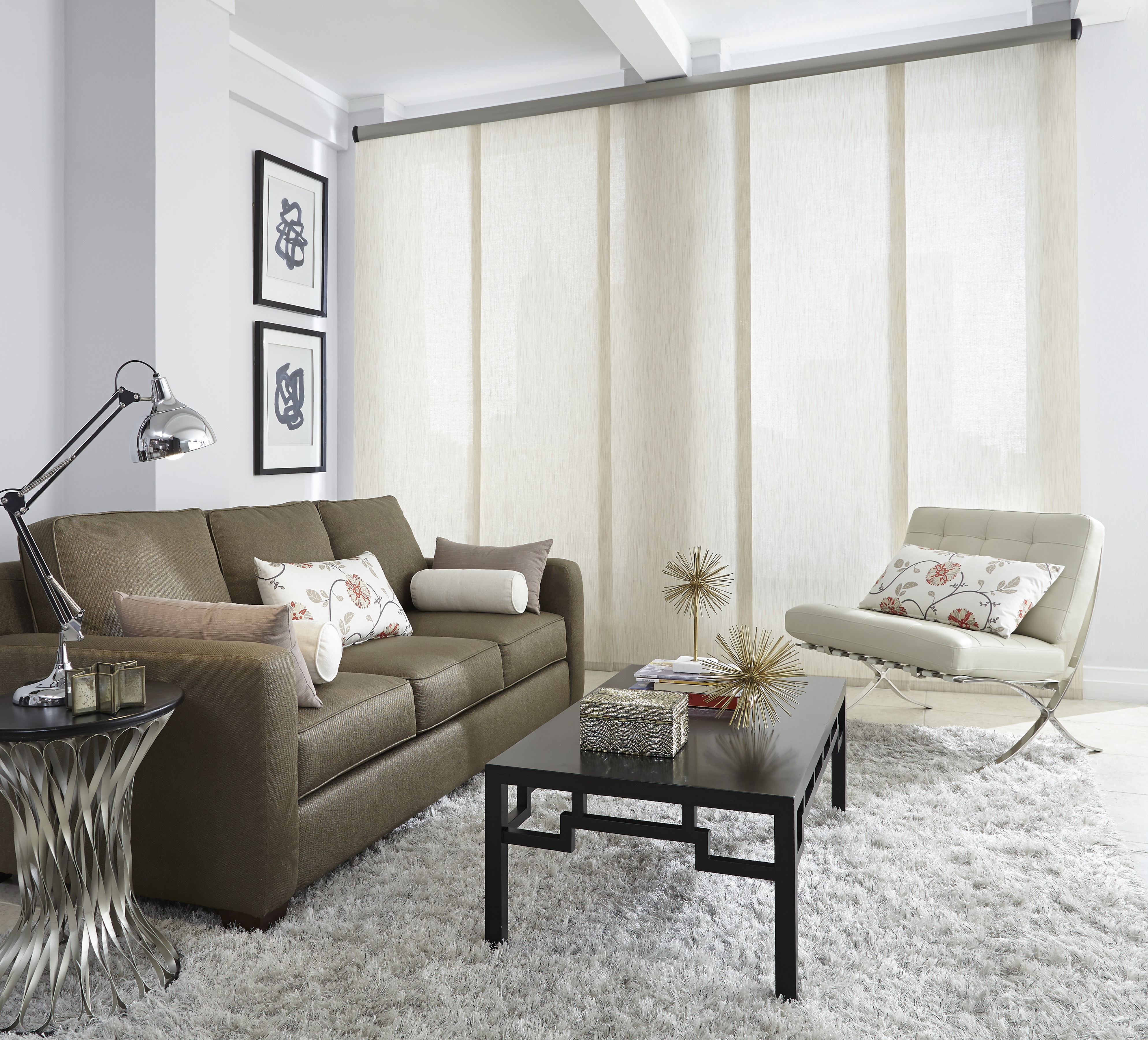 Light-tan colored Genesis® Panel Track System in a room with a brown couch, white chair, and Interior Masterpieces® Custom Pillows