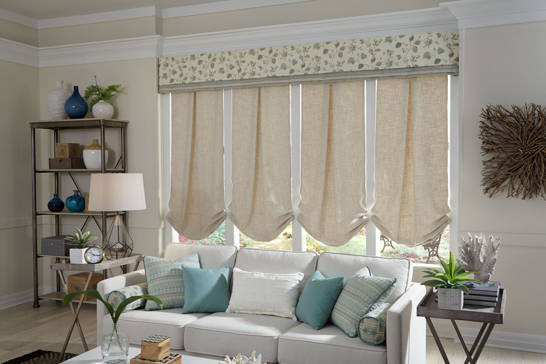4 tan Interior Masterpieces® fabric shades with a wide fabric cornice spanning all four behind a gray couch with accent pillows