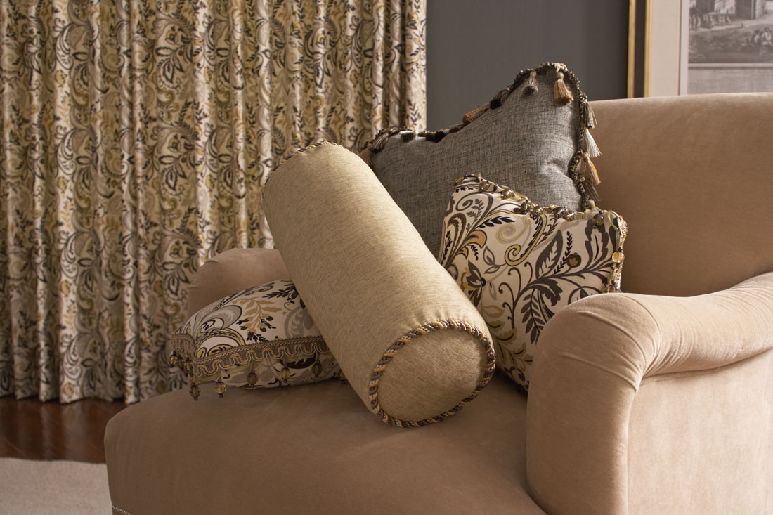 Interior Masterpieces® golden tan Floral Drapery in a room with a chair that has several Interior Masterpieces® Custom Pillows in light tan and gray with Embellishment Trimming