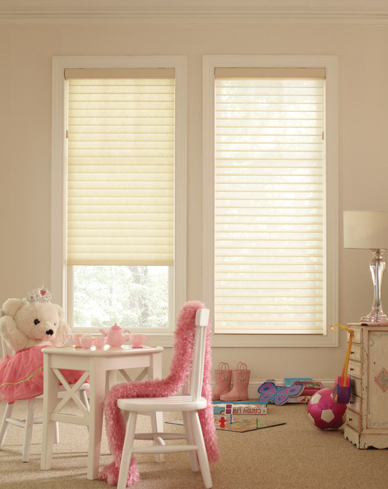 Two white Tenera® Sheer Shades in a kid's room with a little white table and teddy bear with a pink tea set, dress, and scarf