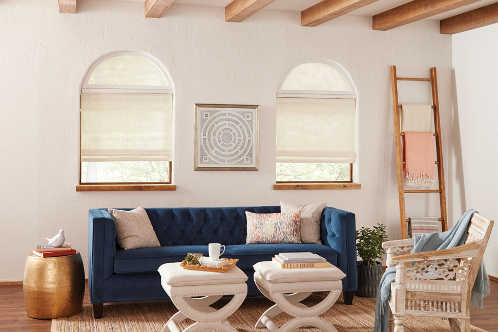 white Manh Truc® Woven Wood Shades with half circle Custom Shapes above them and Palladian Shelves between in a room with a blue couch and Interior Masterpieces® custom pillows and white tables