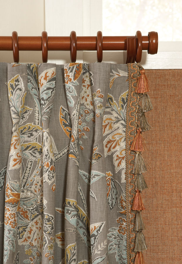 Close up view of dark orange fabric shade and gray floral patterned Interior Masterpieces® draperies with embellishment trimmings and custom dark wooden rod with finials, rings, and support bracket