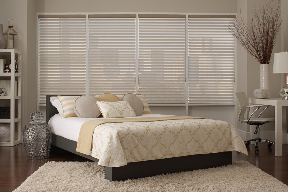 several tan Tenera® Sheer Shades behind a large bed with tan and yellow Interior Masterpieces® Custom Bedding and Pillows