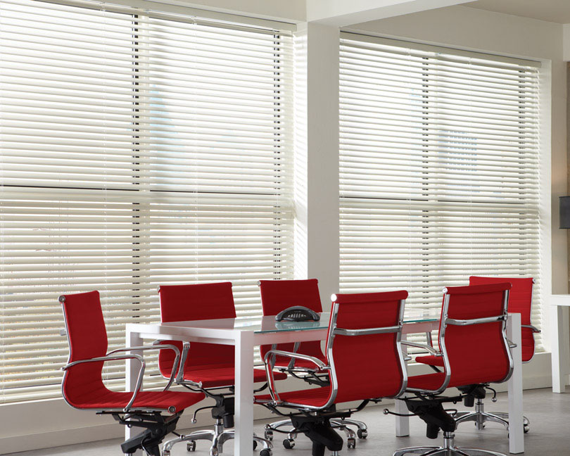 Several large white Classic Collection® Aluminum Blinds in an office with red chairs and a table