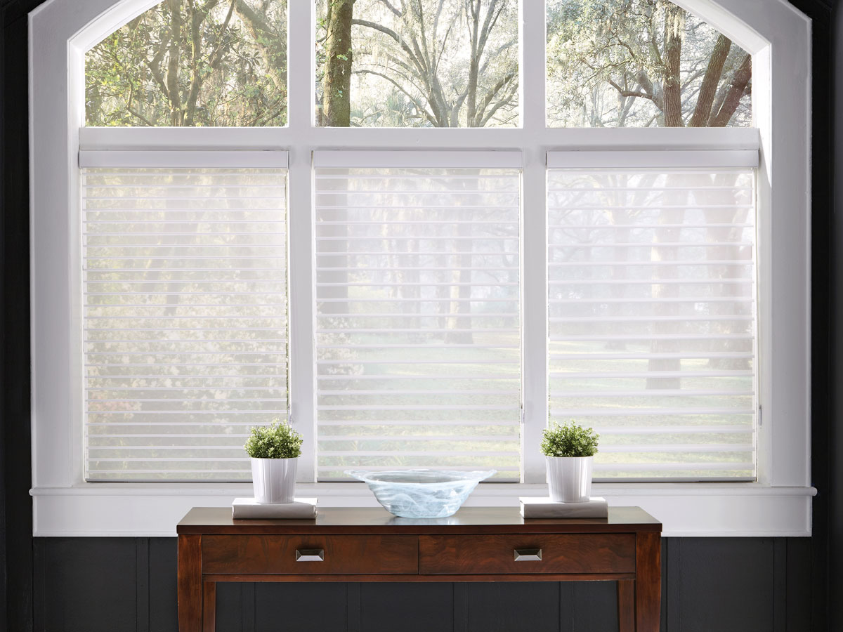 Three white Tenera® Sheer Shades with different vane sizes starting at the smallest on one side with a wooden dark brown table with white plant pots in front of it