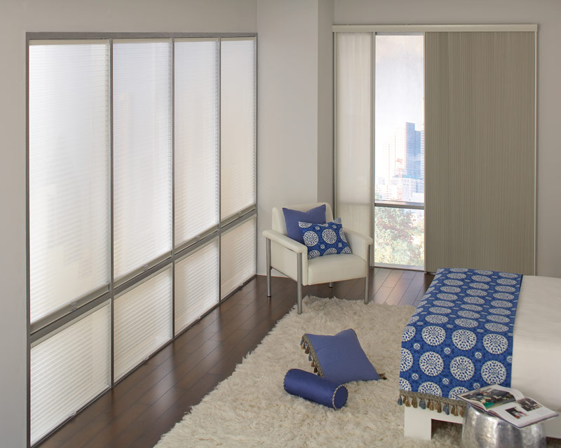several large tan Parasol® Cellular Shades on one wall and a large Glissade sliding panel system on the other in a room with a bed that has blue Interior Masterpieces® bedding and accessories on it