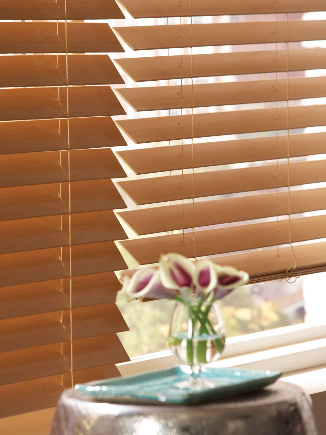 closeup of brown Fidelis® Faux Wood Blinds with a purple flower in the foreground