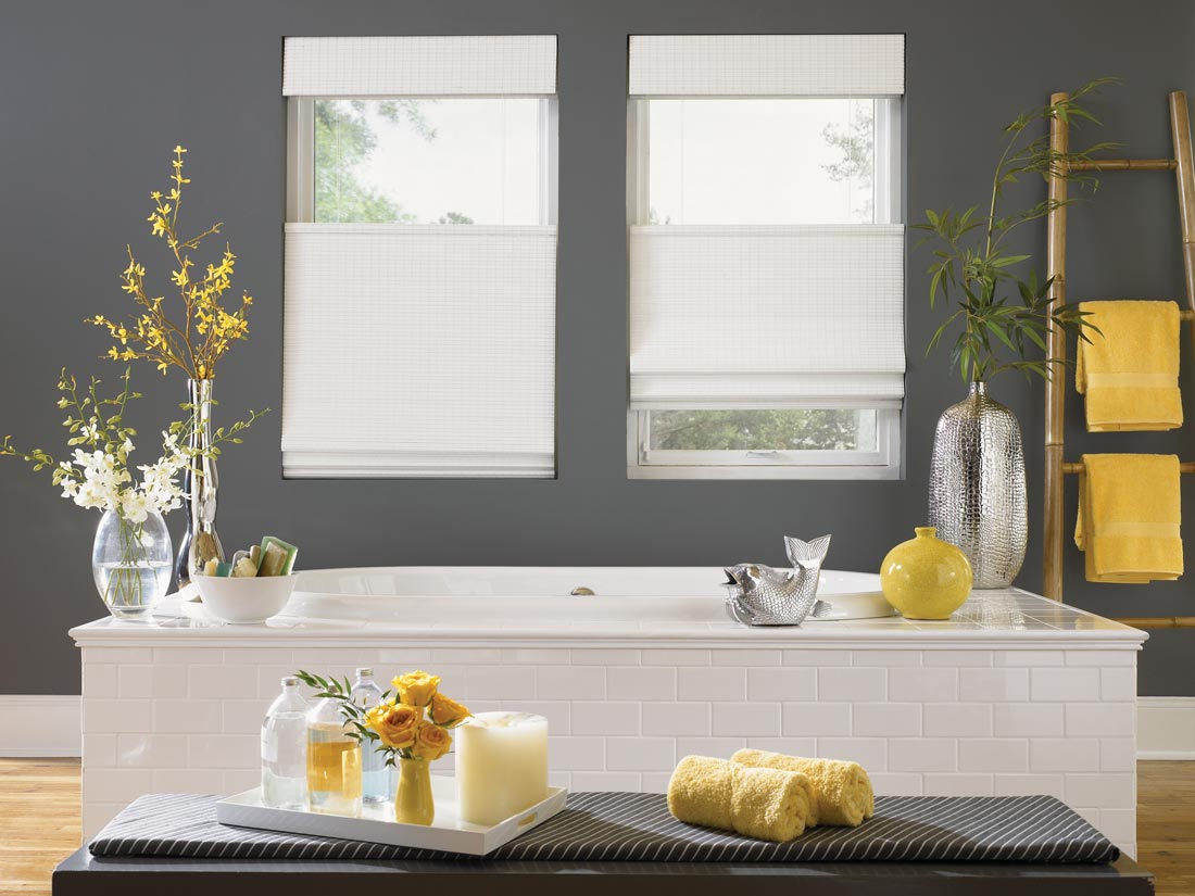 Two white top down, bottom up Manh Truc® Woven Wood Shades in a bathroom with gray walls and yellow decorations around behind a white bath tub