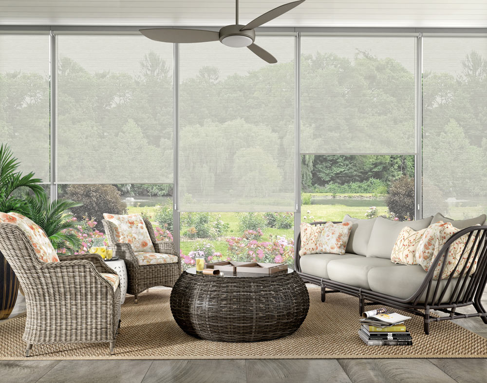 Wide screened in porch area with several light gray Genesis® roller shades and outdoor furniture with Interior Mastepieces® custom pillows in floral prints