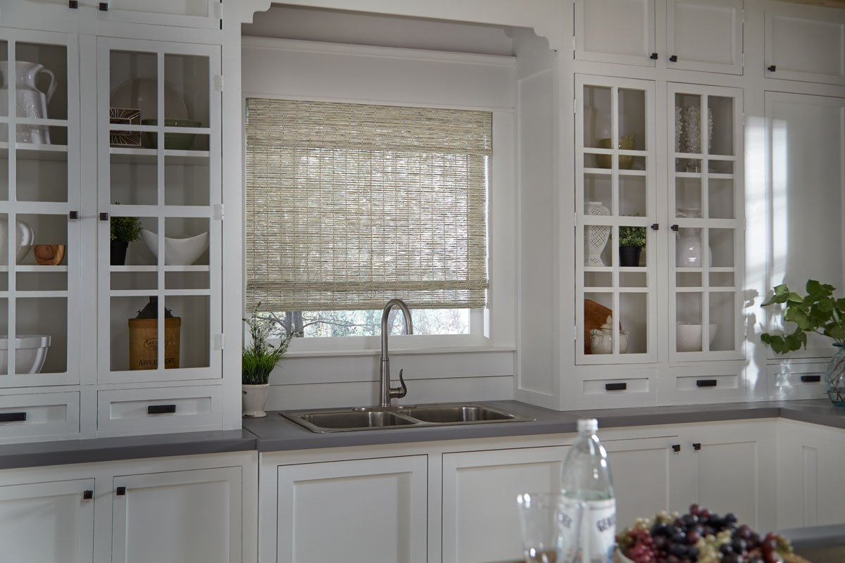 Light colored Manh Truc® Woven Wood Shade behind a kitchen sink and in between cabinets