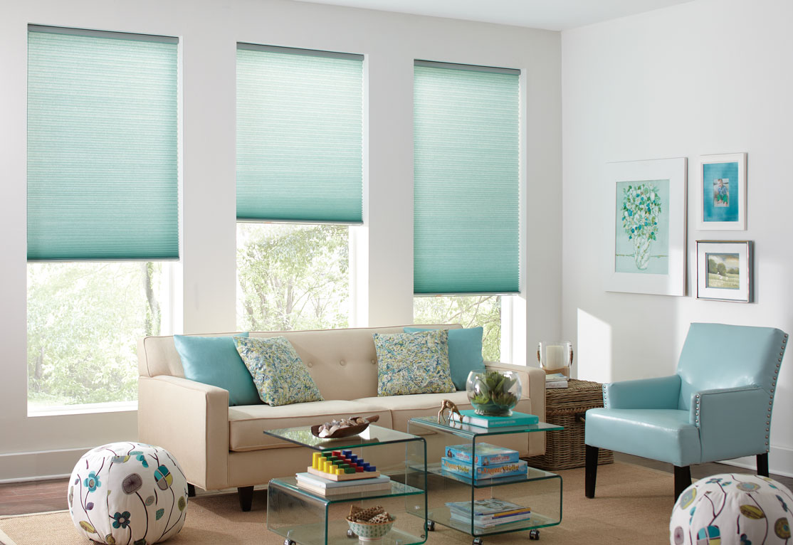 Three Parasol® Cellular shades in a light blue color in front of a tan couch with matching pillows and a blue matching chair