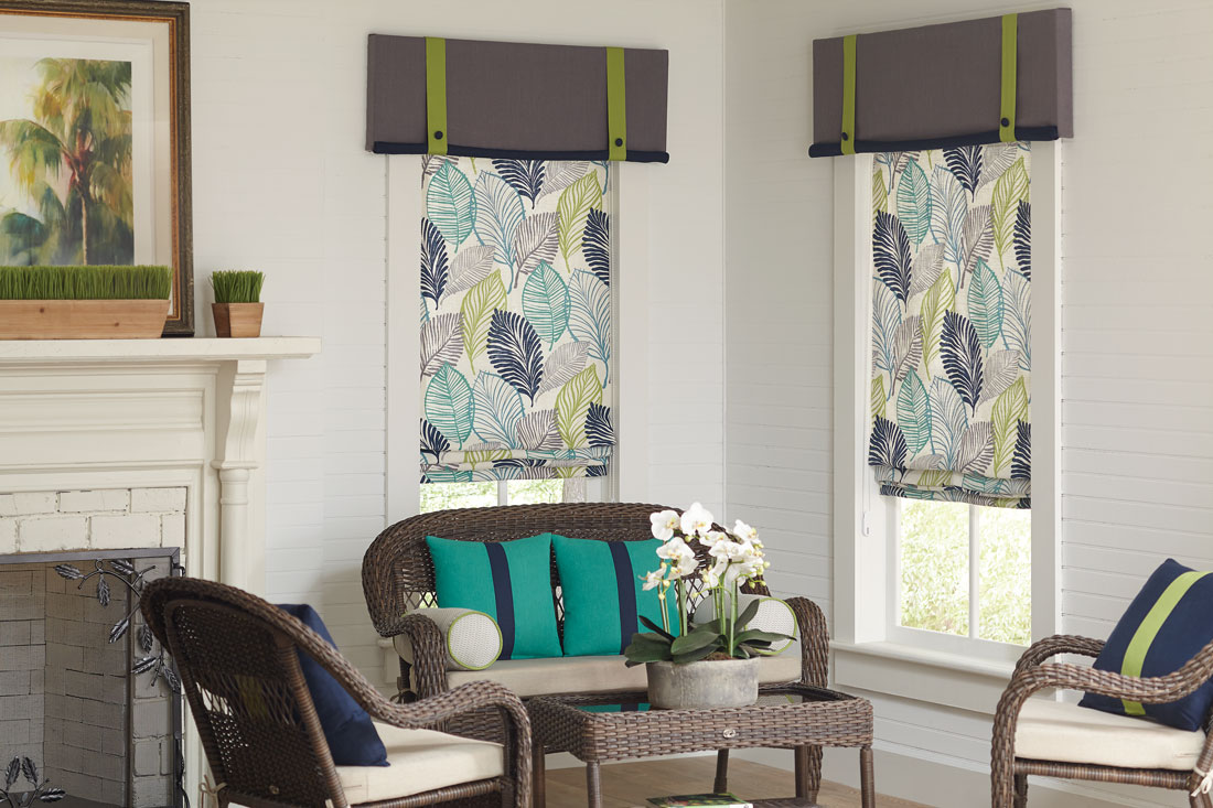 Two blue, teal, yellow, and gray floral patterened Interior Masterpieces® fabric shades with accenting fabric gray and lime green cornices in a room with benches that have teal and blue custom pillows