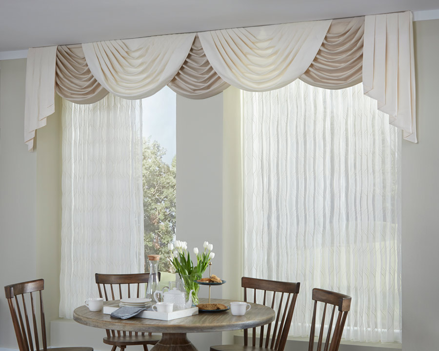 Interior Masterpieces® draperies with festooned draperies valance spanning a dining room wall with a table and chairs in front