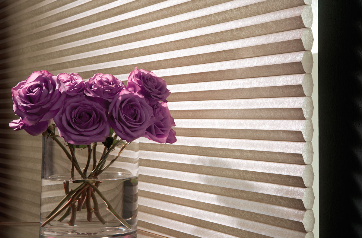 Close up of a tan Parasol® Cellular shade material with purple roses in front