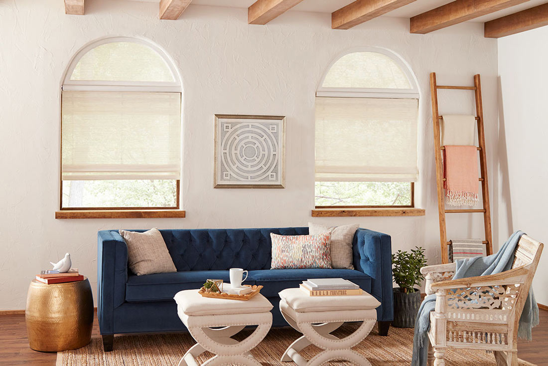 two white Manh Truc® Woven Wood Shades with  half circle Custom Shapes on top & Palladian Shelf in between behing a blue couch with custom pillows