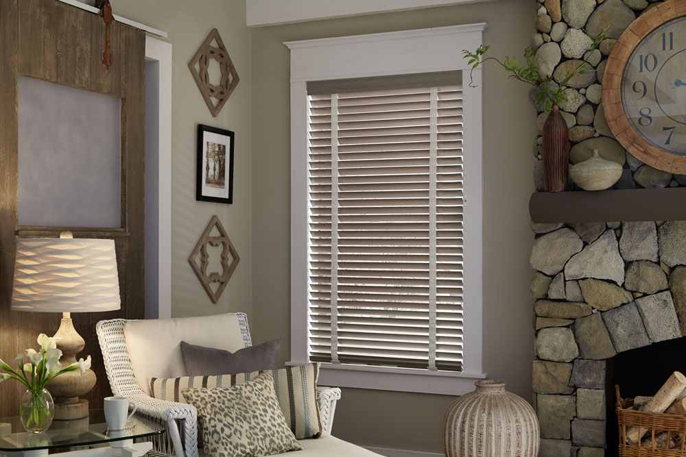 Gray Heartland Woods® Wood Blinds with white Decorative Tape next to a chair with custom pillows from the Interior Masterpieces® line