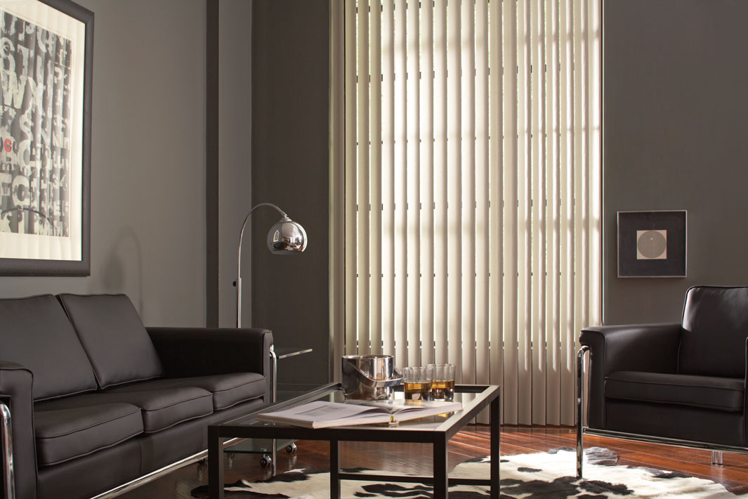 White Discoveries® Vertical Blinds in a room with gray walls and black furniture