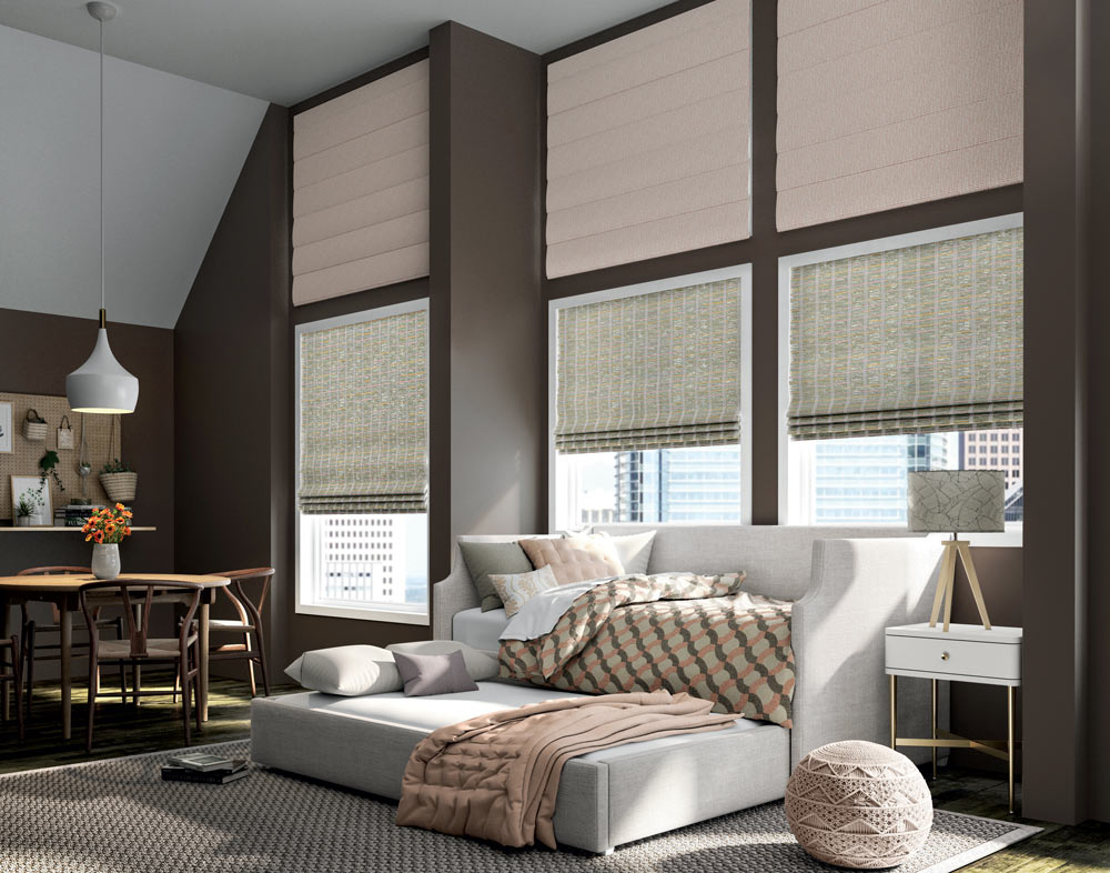 light green Motorized Manh Truc® Woven Wood Shades & pale pink Interior Masterpieces® Fabric Shades against brown walls behind a couch and pull out sleeper with Custom Bedding in pale pink, green, and brown