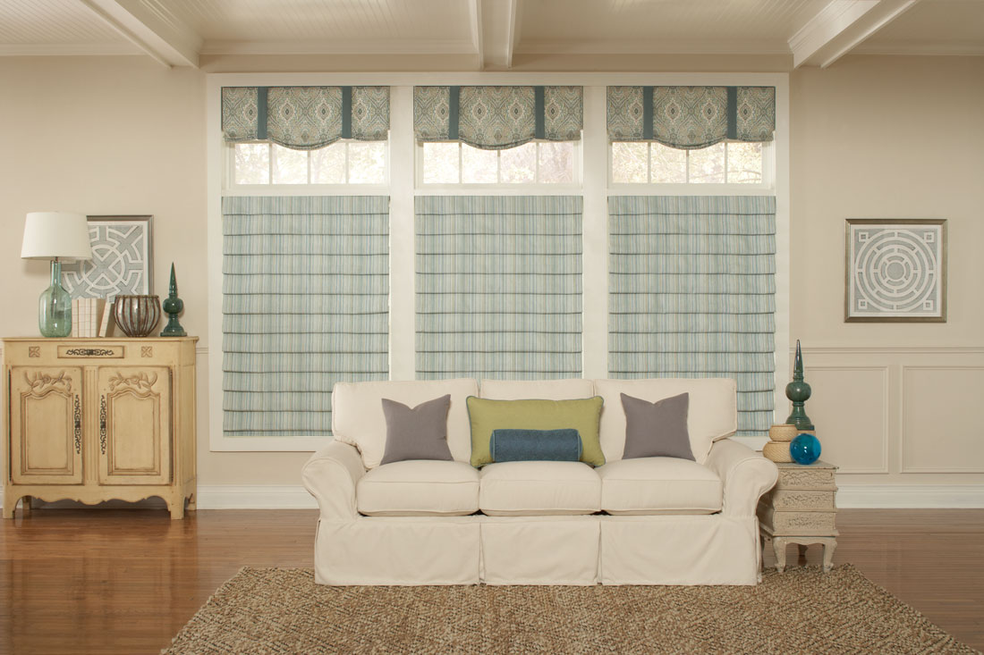 three light greenish blue striped Interior Masterpieces® fabric shades with fabric wrapped cornices above each behind a couch with custom gray, yellow, and blue pillows