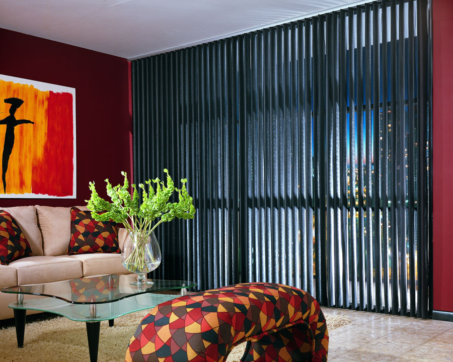 Black Discoveries® Vertical Blinds in a large picture window against a red wall with tan furniture and a red and orange painting