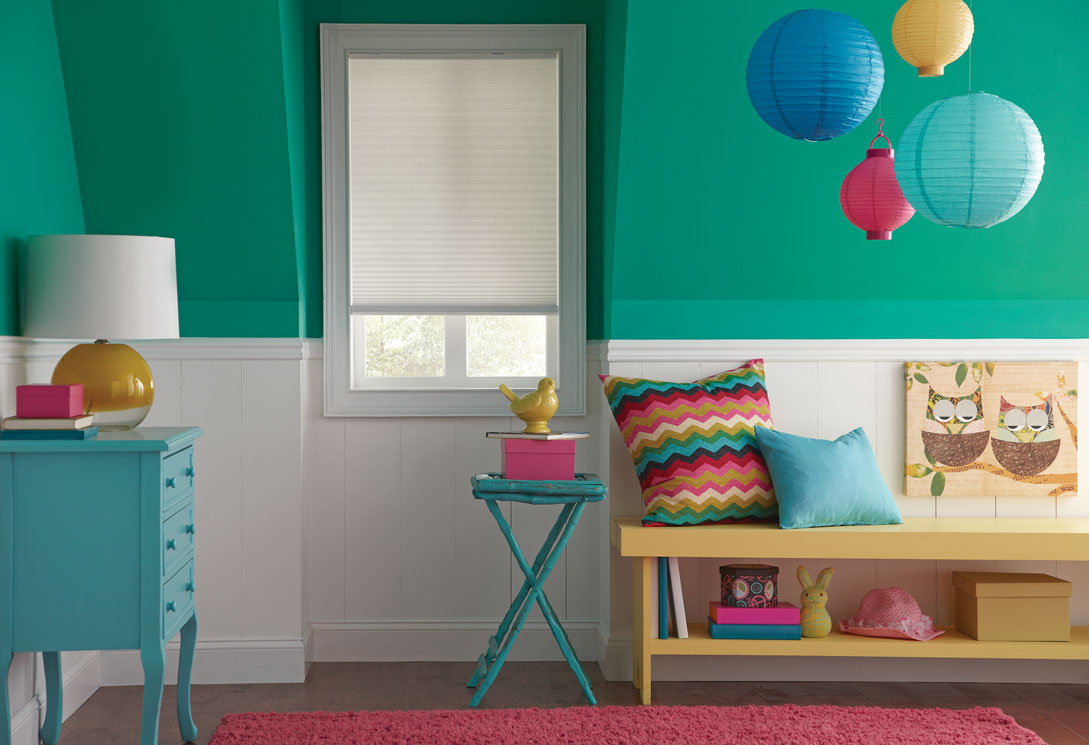 Light colored Parasol® Cordless shade in a window against a green wall in a child's room with brightly colored blue furnishings and multicolored pillows around