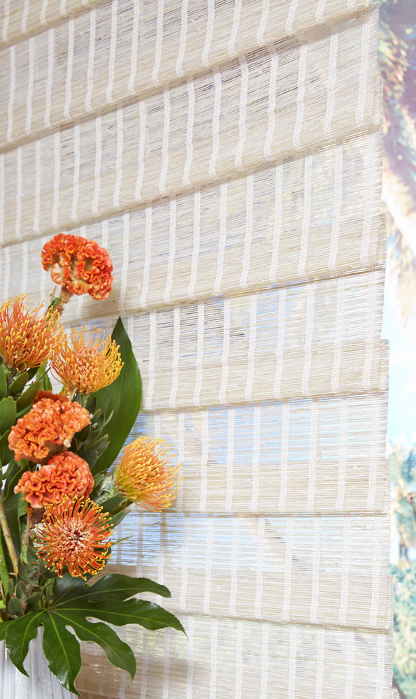 close up of white colored of Manh Truc® Woven Wood Shades with orange flowers in the foreground