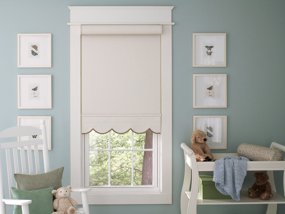 light tan Genesis® Roller Shades with Scalloped Hem and brown Decorative Trim against a white frame with blue walls in a child's room with a changing table and stuffed animals nearby